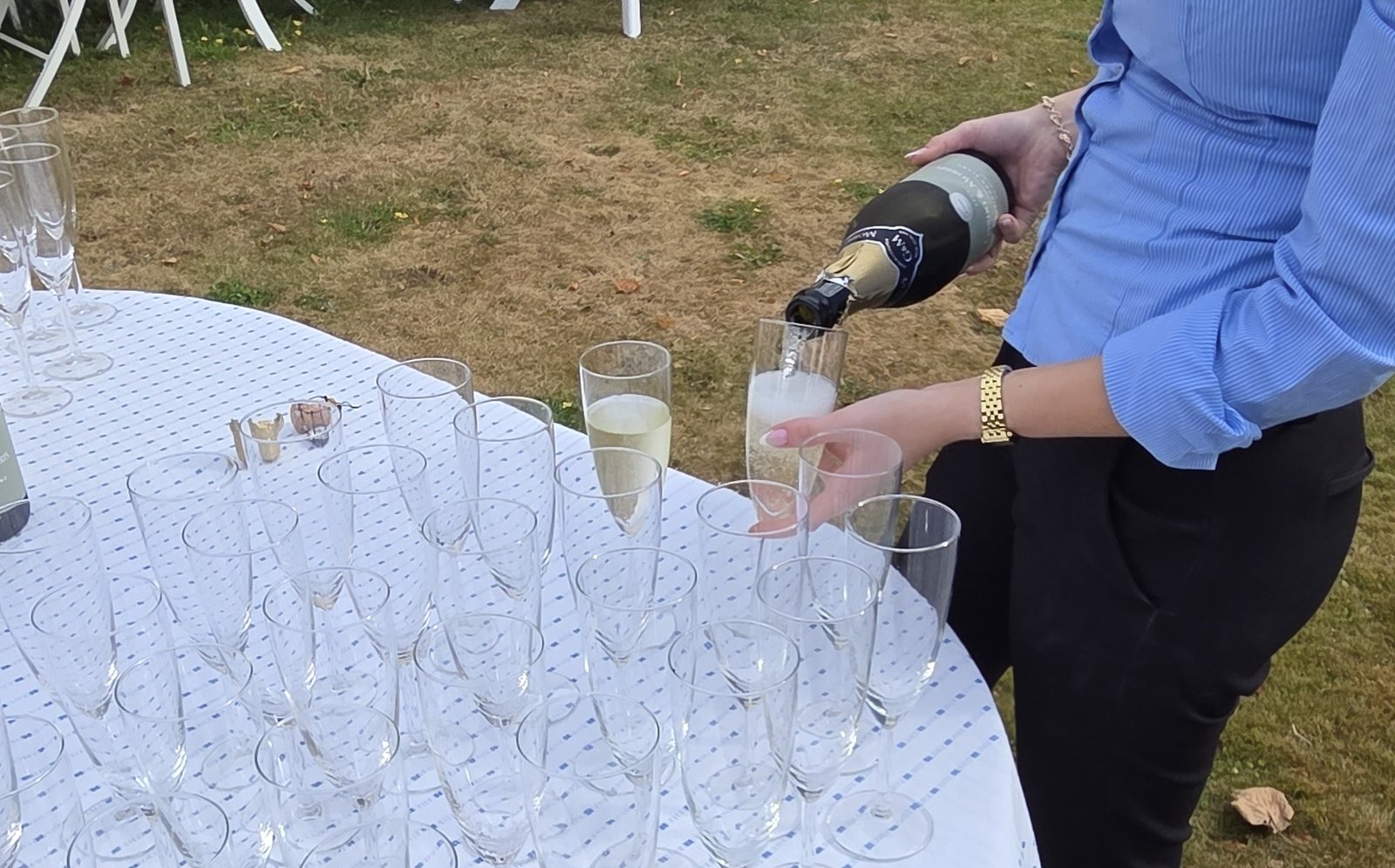 Champagne hälls upp i glas på ett dukat bord i trädgården.