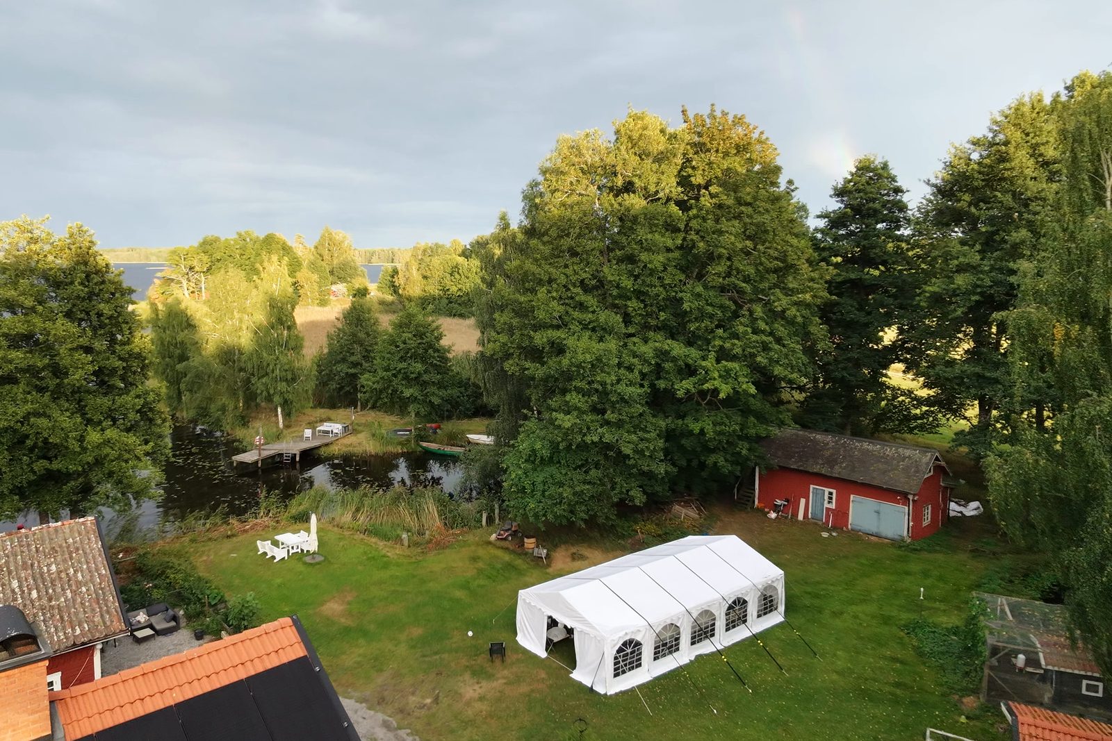 Vitt partytält på gräsmattan intill röda uthus.